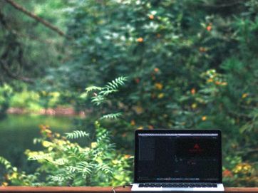 Laptop mit schwarzem Bildschirm auf einer Fensterbank, vor dem Fenster üppiger Wald