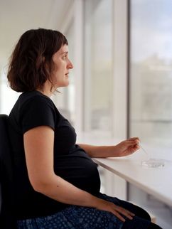 Eine schwangere Frau mit einer Spritze und einer Petrischale vor einem Fenster.